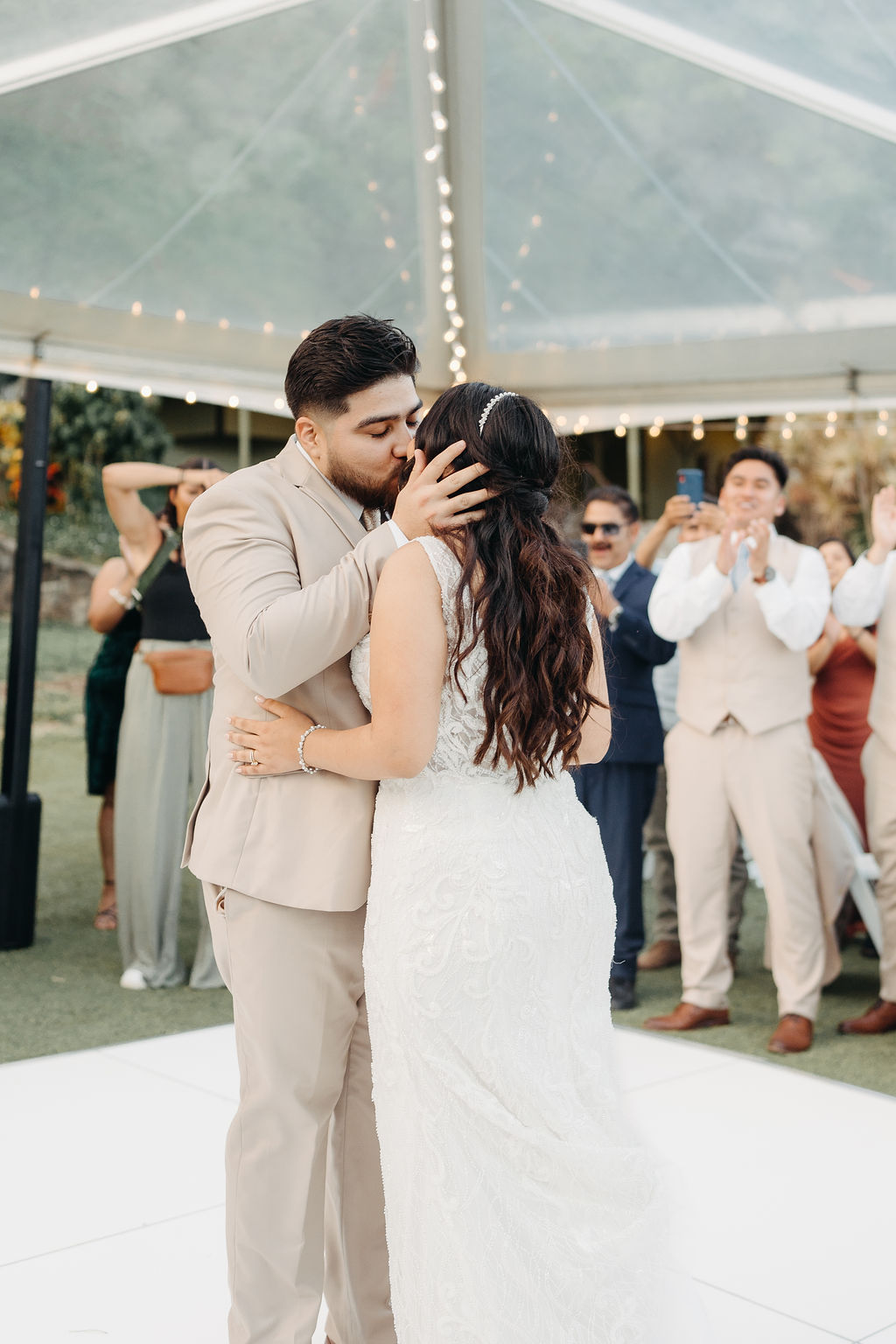 A couple dressed elegantly shares a dance on a white platform under a clear tent, with seated guests in the background at Kualoa ranch