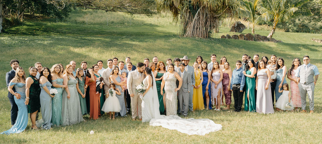 A large group of people, dressed in formal attire, poses outdoors on a grassy area with trees in the background.