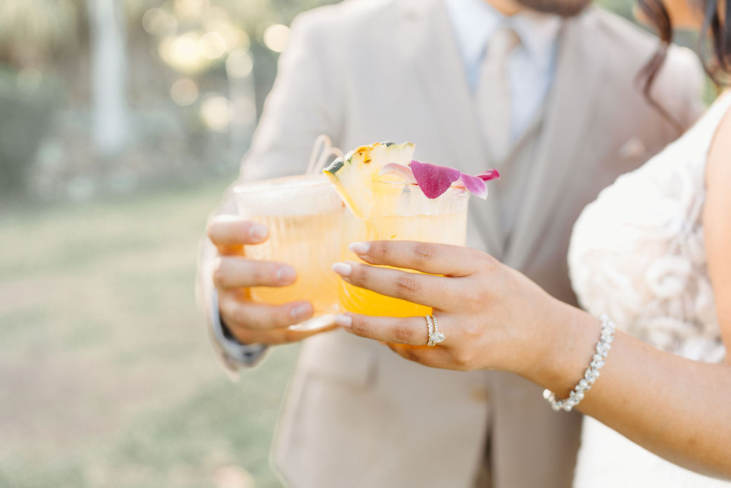 A person pours drinks into cups at a bar with golden shakers, while three people in the background are smiling.