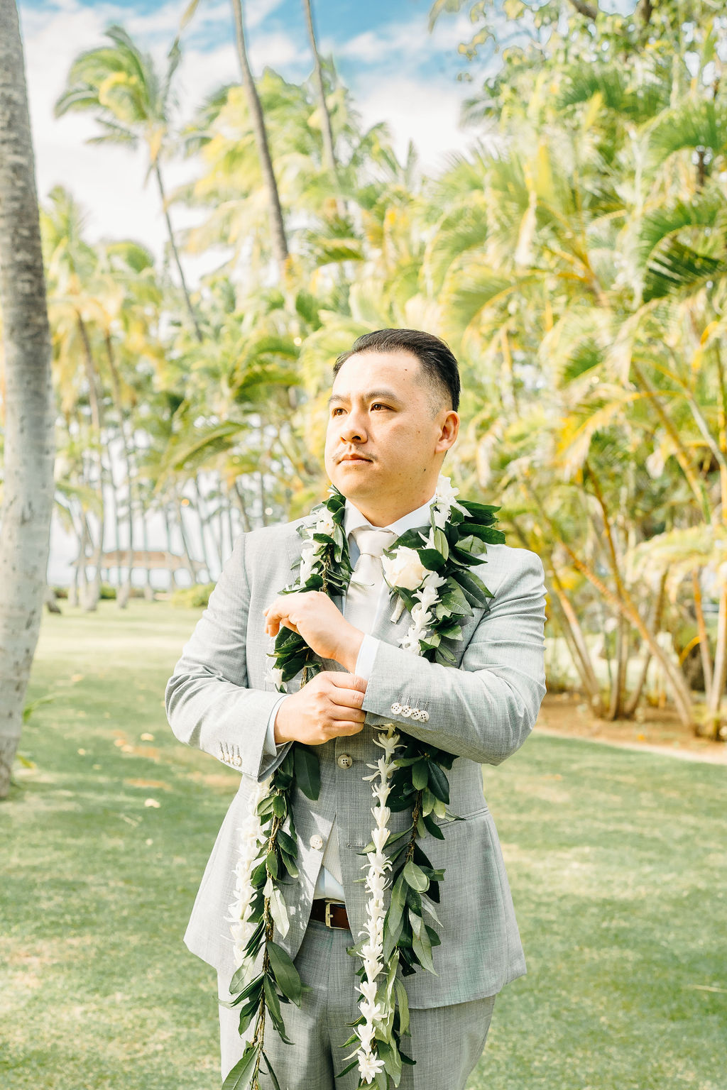 A group of groomsmen lifts the groom on their shoulders, smiling and wearing leis, posed in a sunny outdoor setting with palm trees for a wedding at Wedding at Lanikuhonua Cultural Institute