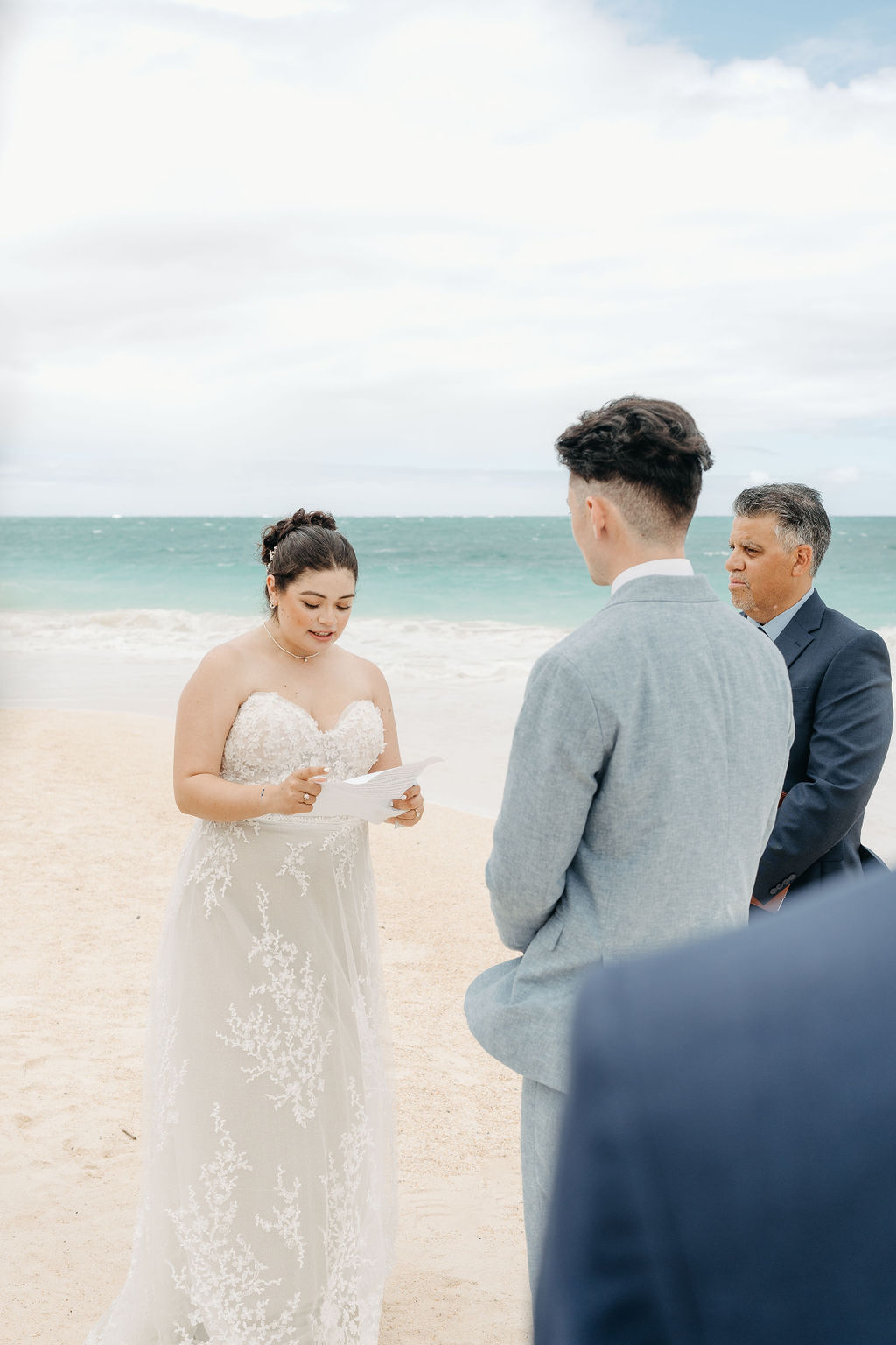 Close-up of a groom placing a ring on the bride's finger during a wedding ceremony. Bridesmaids in blue dresses are visible in the background.