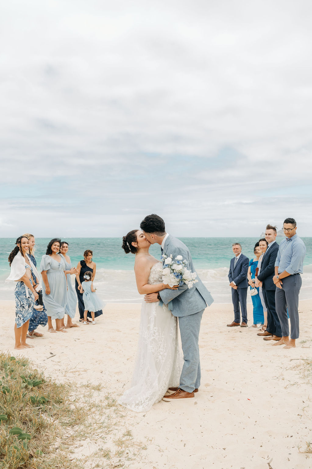 A couple is kissing on a beach during a wedding ceremony, surrounded by a small group of people for a beach wedding in oahu