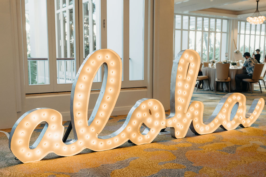 Large illuminated sign spelling "aloha" inside a room with windows and event tables for a wedding at the four seasons in oahu