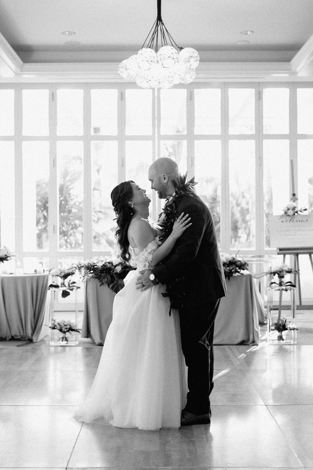 A bride and groom kiss on a dance floor in a well-lit room, with white flowers and draped tables in the background for a wedding at the four seasons in Oahu