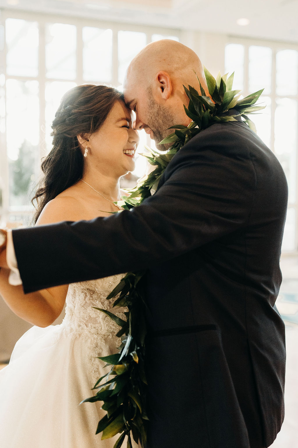 A bride and groom kiss on a dance floor in a well-lit room, with white flowers and draped tables in the background for a wedding at the four seasons in Oahu