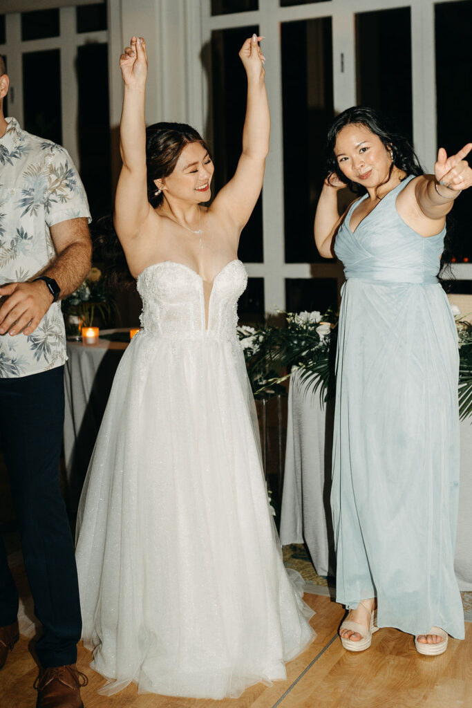 People dancing energetically at a wedding reception with a woman in a white dress leading the dance.