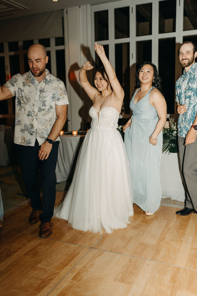 People dancing energetically at a wedding reception with a woman in a white dress leading the dance.