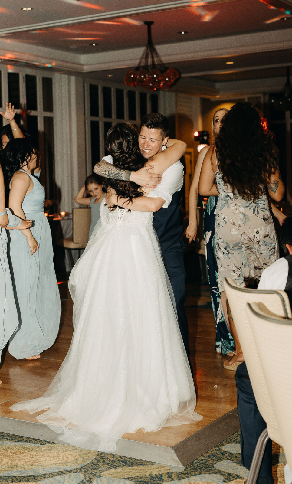 People dancing energetically at a wedding reception with a woman in a white dress leading the dance.