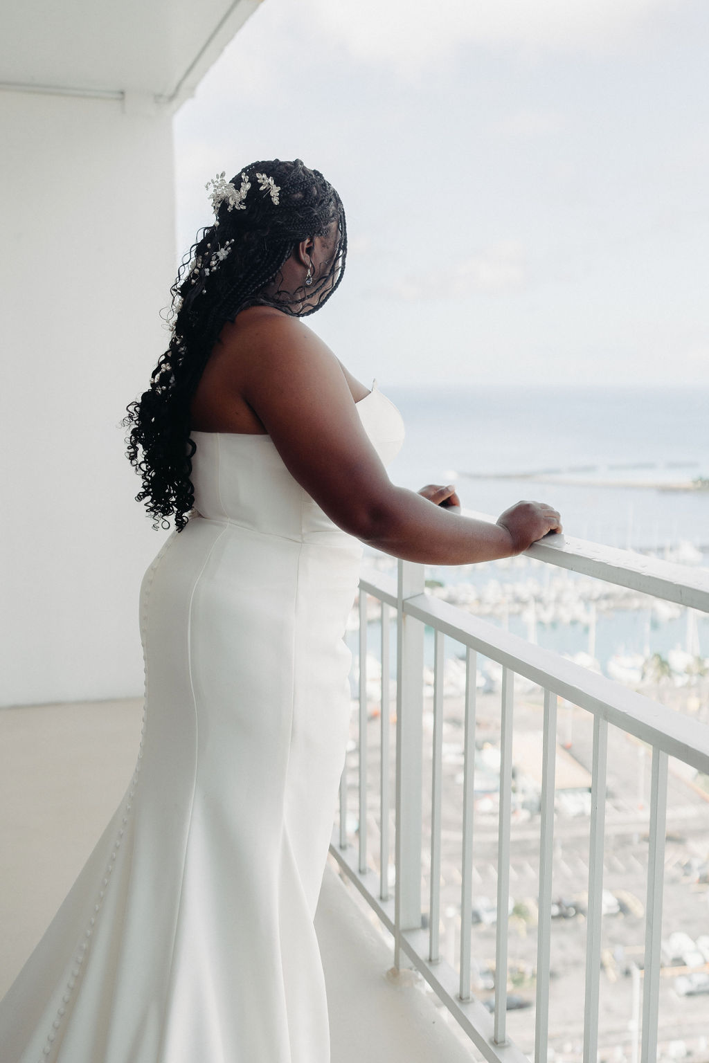 Bride in a white wedding dress adjusts her earring while looking out a window.