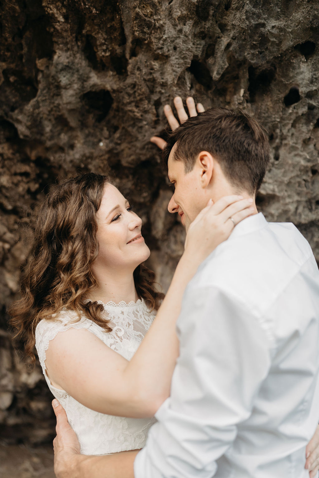 A couple embraces on a cliffside overlooking mountains and a body of water, under a partly cloudy sky for their hawaii elopement