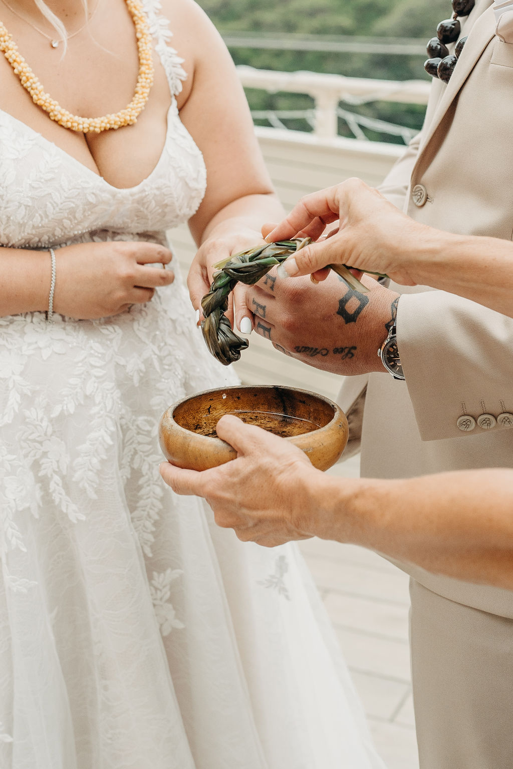 A bride and groom stand under a decorated wooden arch outdoors, facing each other as the bride reads from a paper. Mountains and greenery are visible in the background for a wedding at queen kapiolani hotel