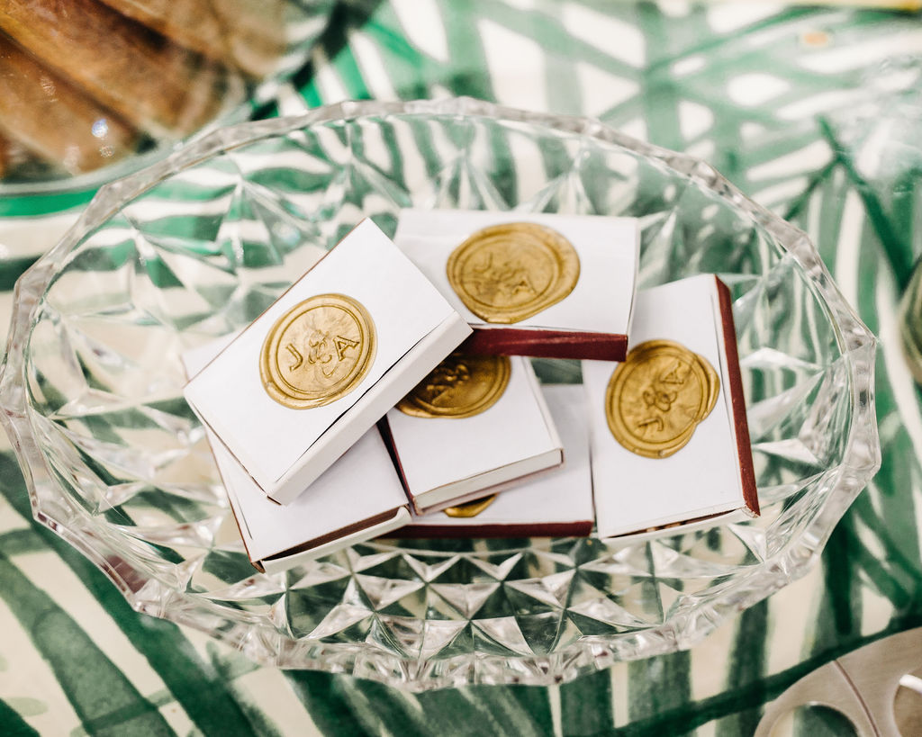 A glass bowl contains several small white boxes with gold wax seals, arranged on a green and white patterned surface.