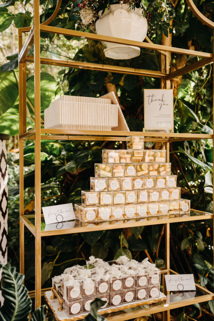 Gold shelves displaying stacked gift boxes and small white packages, set against a background of lush green foliage.