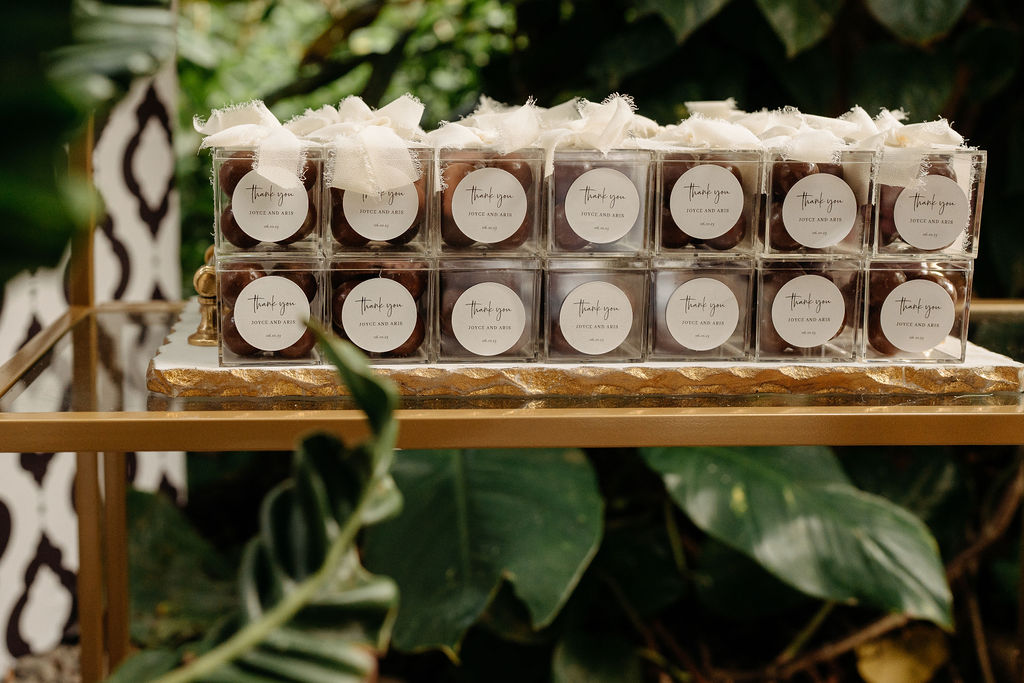 Gold shelves displaying stacked gift boxes and small white packages, set against a background of lush green foliage.