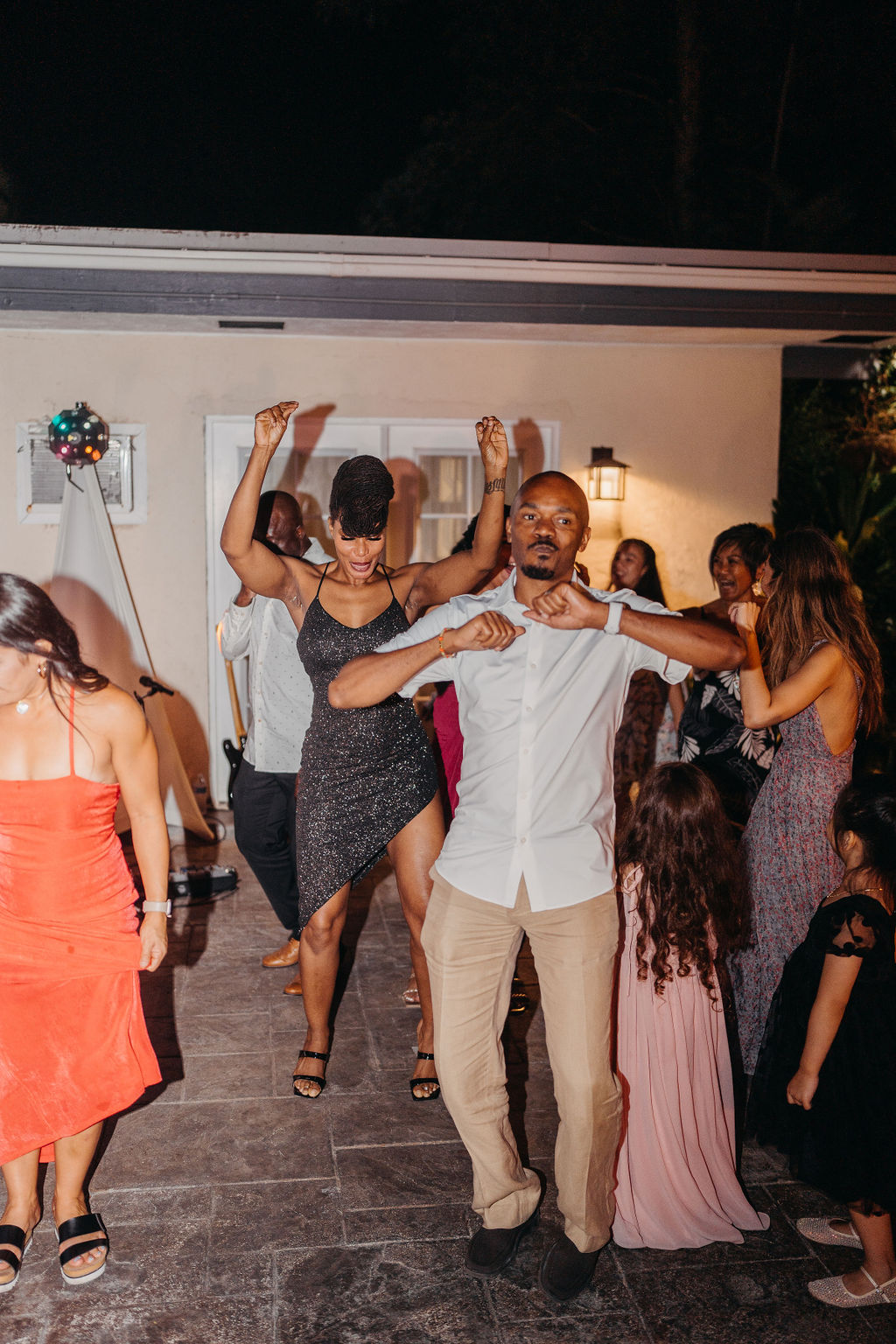A group of people dressed in formal attire dance together at an outdoor backyard wedding in Oahu