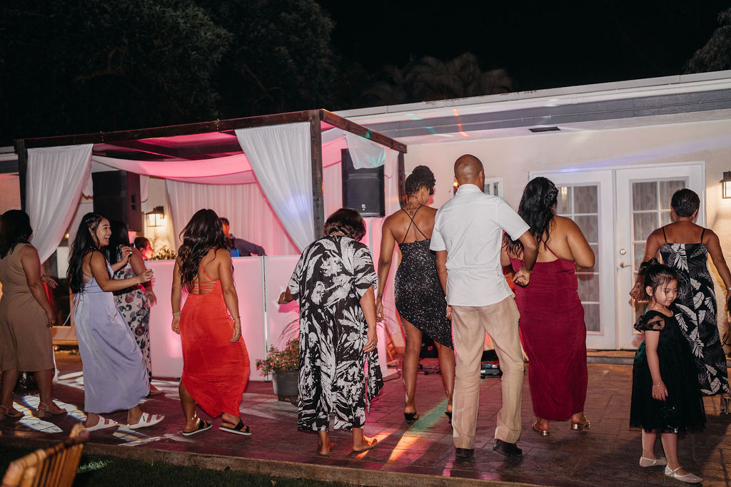 A group of people dressed in formal attire dance together at an outdoor backyard wedding in Oahu