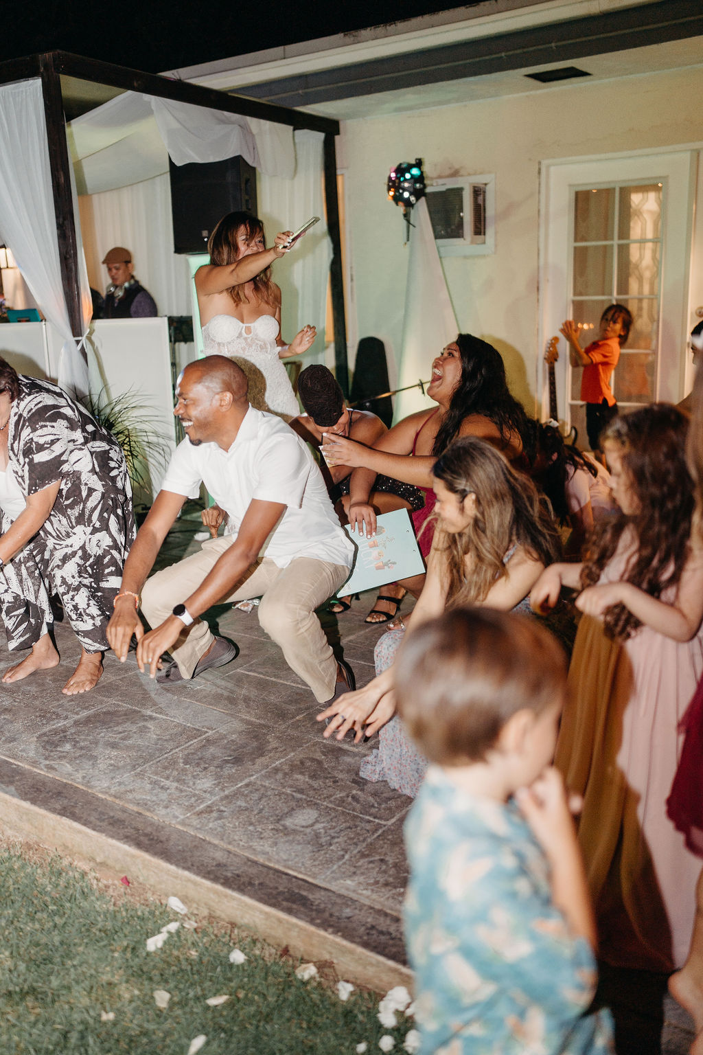 A group of people dressed in formal attire dance together at an outdoor backyard wedding in Oahu