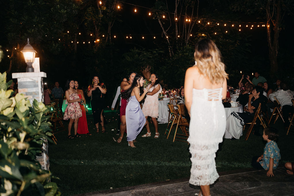 A group of people dressed in formal attire dance together at an outdoor backyard wedding in Oahu