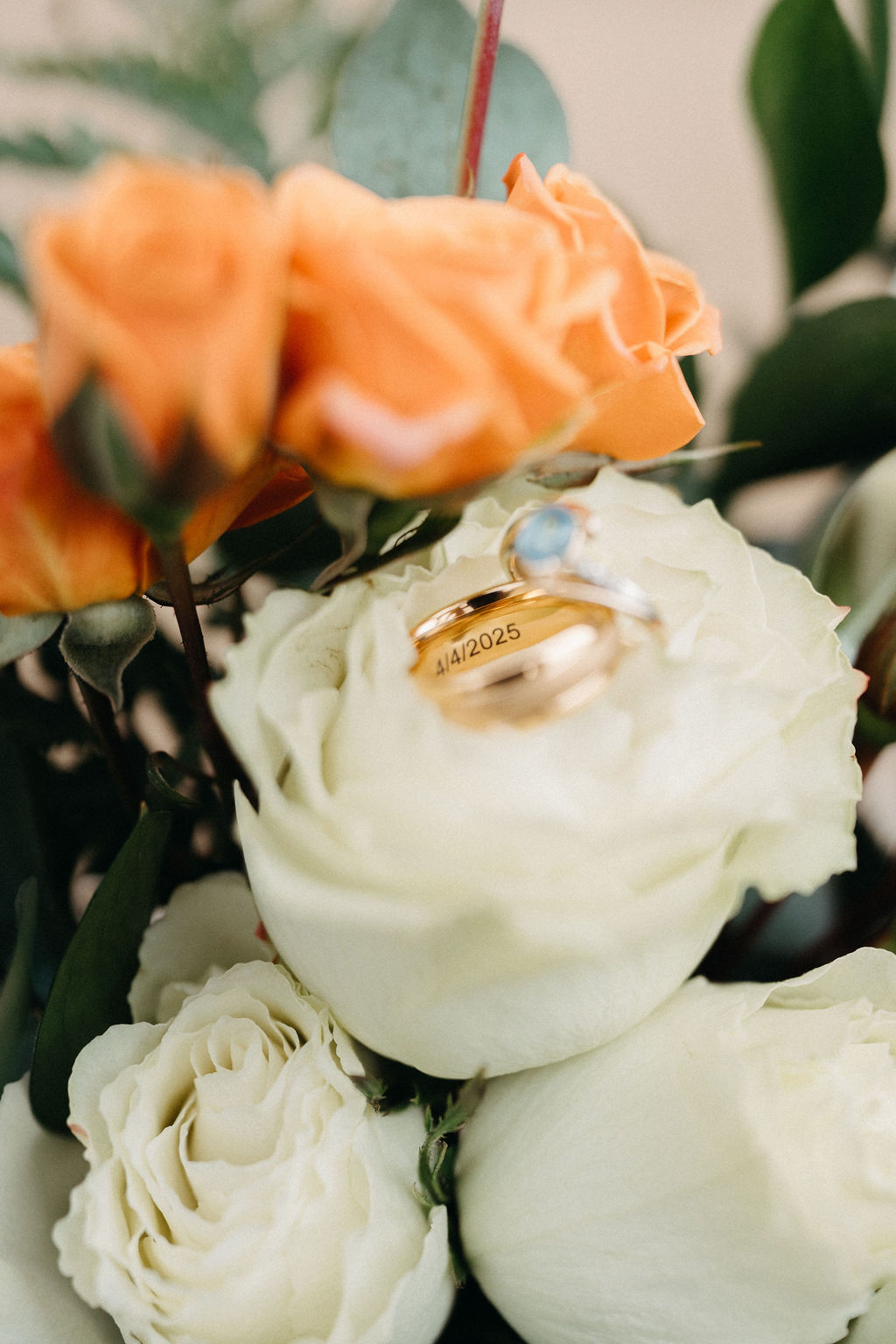Two rings, one gold and one silver with a blue stone, rest on handwritten notebook pages with leafy branches nearby.