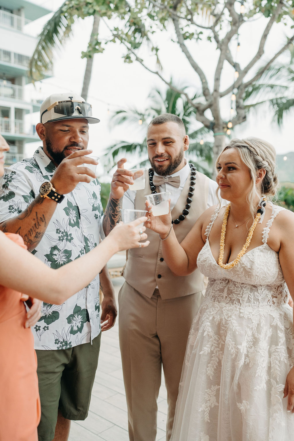 A bride and groom stand with their family in front of a wooden wedding arch decorated with greenery and flowers, outdoors with a mountain view.