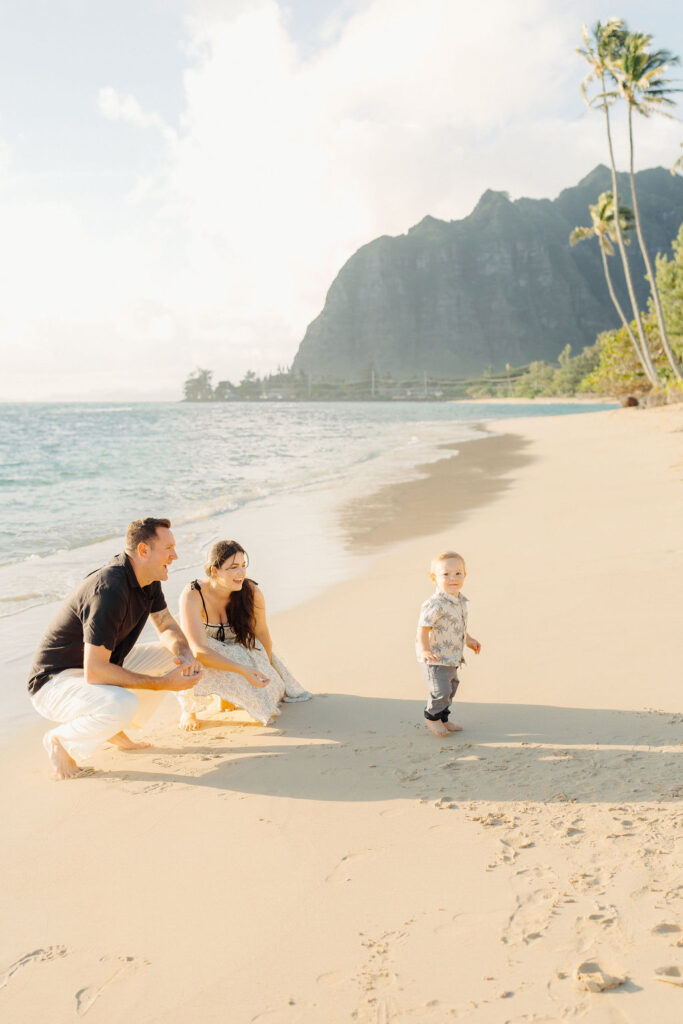 family takes Hawaii family photos on Kaaawa beach at sunset with a toddler