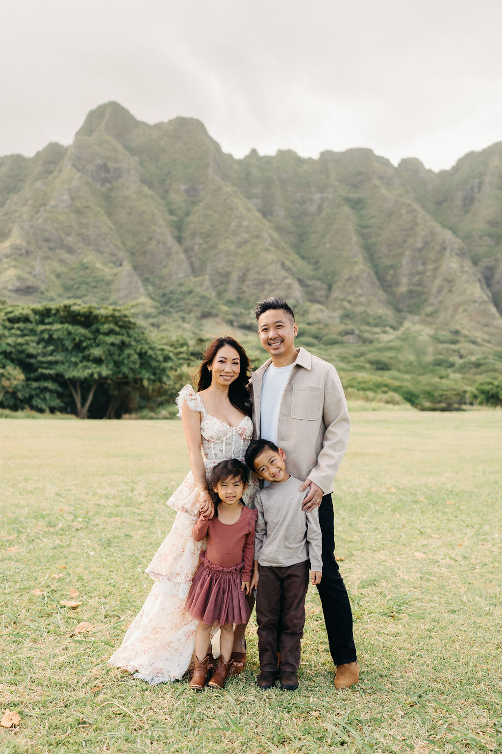 A family of four poses together on a grassy field with green mountains in the background for their mini family session