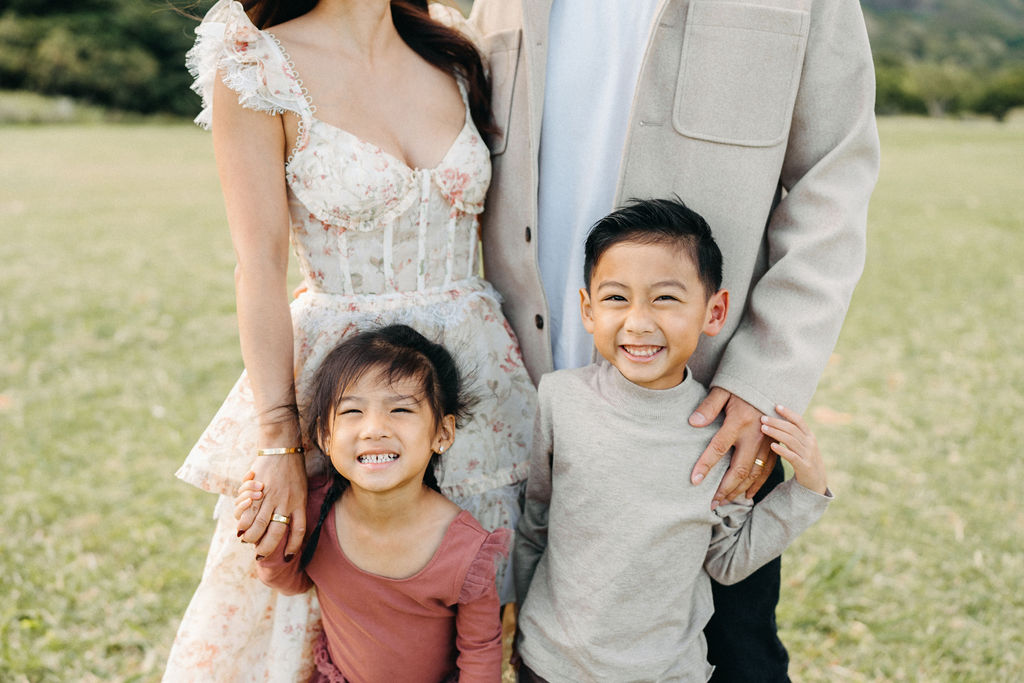 A family of four poses together on a grassy field with green mountains in the background for their mini family session