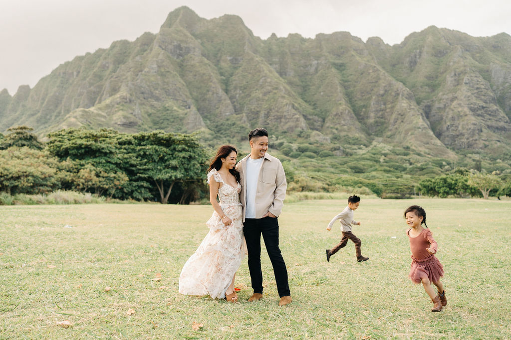A family of four poses together on a grassy field with green mountains in the background for their mini family session