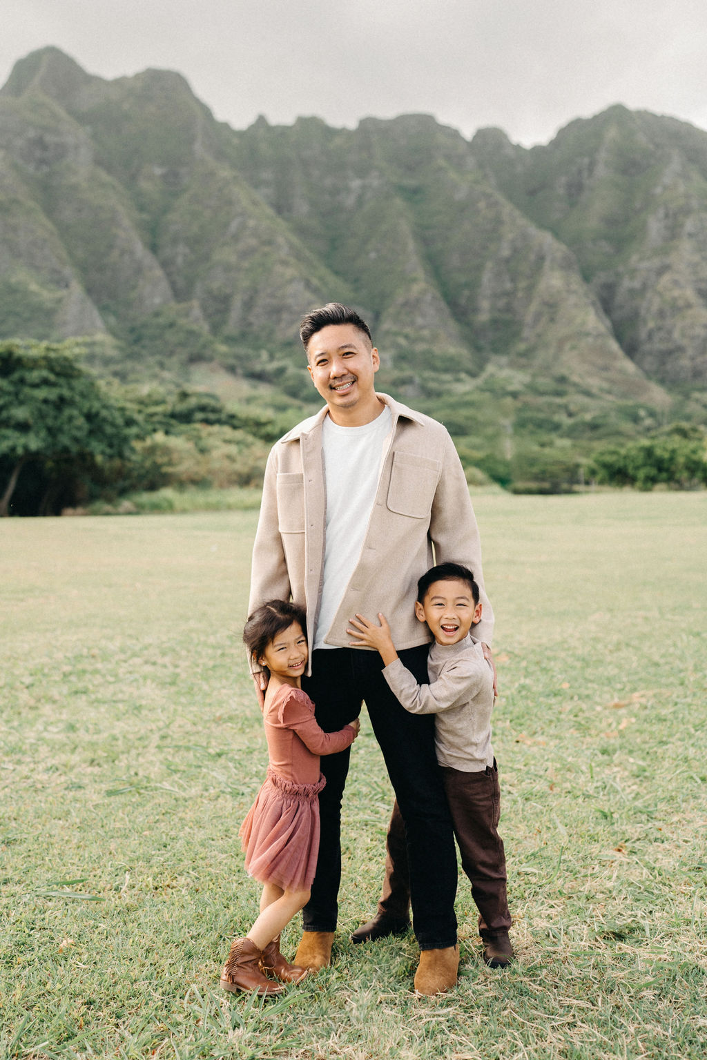 A family of four poses together on a grassy field with green mountains in the background for their mini family session