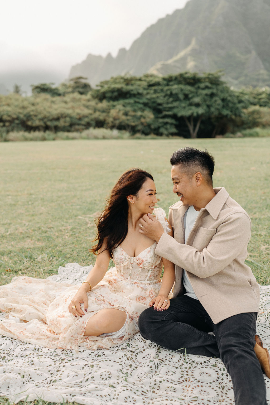 A family of four poses together on a grassy field with green mountains in the background for their mini family session