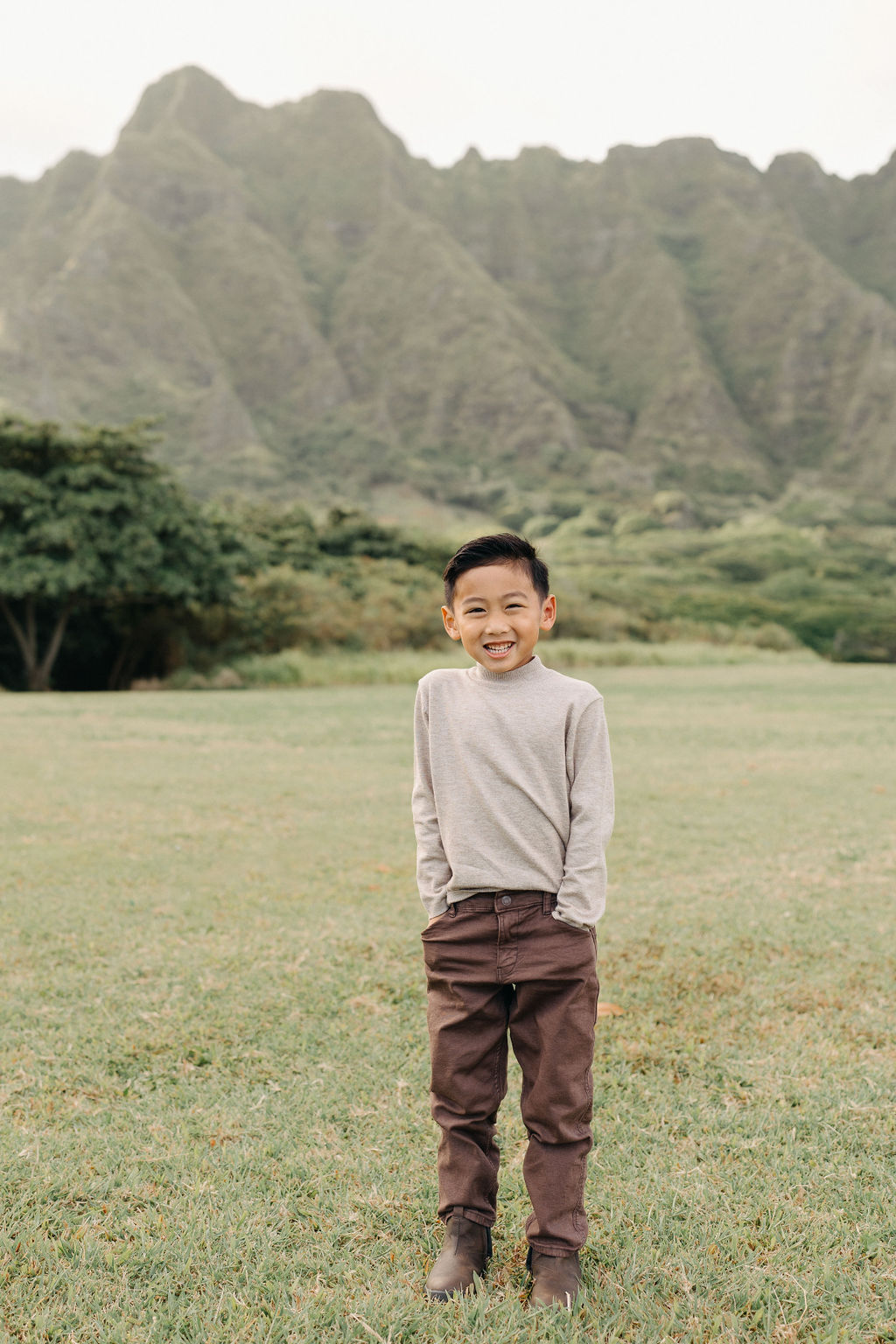 A family of four poses together on a grassy field with green mountains in the background for their mini family session
