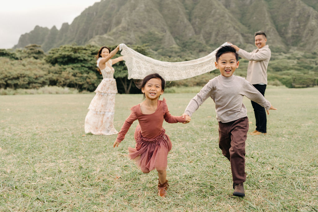 A family of four poses together on a grassy field with green mountains in the background for their mini family session
